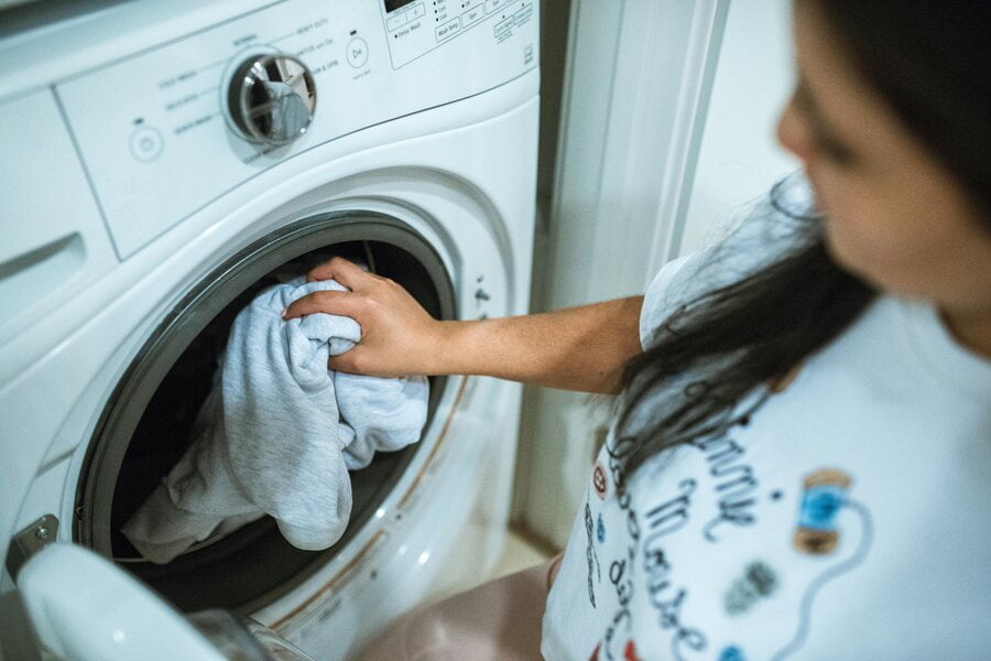 a woman puts her clothes in the washing machine